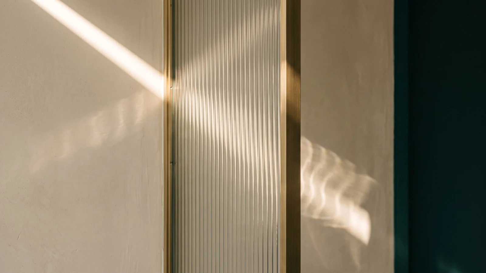 A line of warm light across reeded glass, a brass frame and a petrol wall